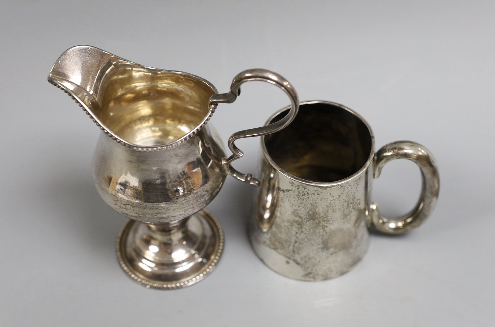 A George III silver inverted pear shaped cream jug, marks rubbed, 72mm and a later silver christening mug.